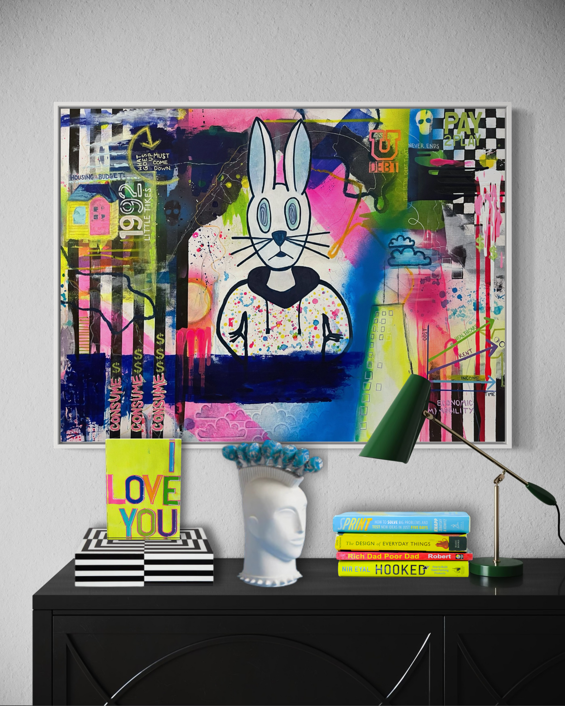 An original 30"x40" painting by Chicago Artist Sarah Henry in abstract expressionist style with graffiti and street art elements hangs on a white wall. The art showcases the struggle of economic mobility for the working, middle, and lower classes with visual commentary on the housing crises, student loan debt, global warming, economic volatility, increasing cost of living, and flat wage growth. It sits above decor from Jonathan Adler on a black dresser.