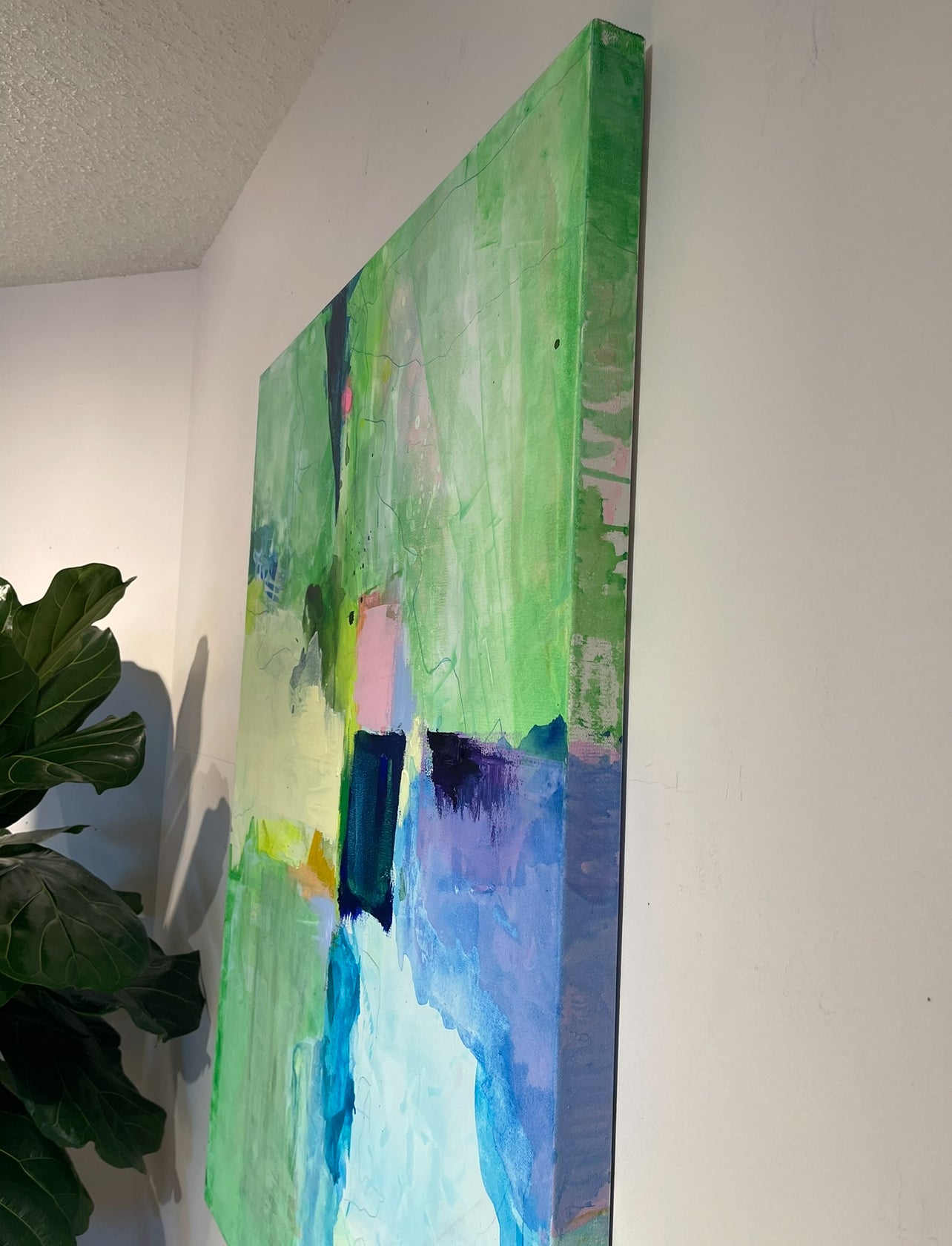 Colorful abstract painting on a white wall with a plant to the left.