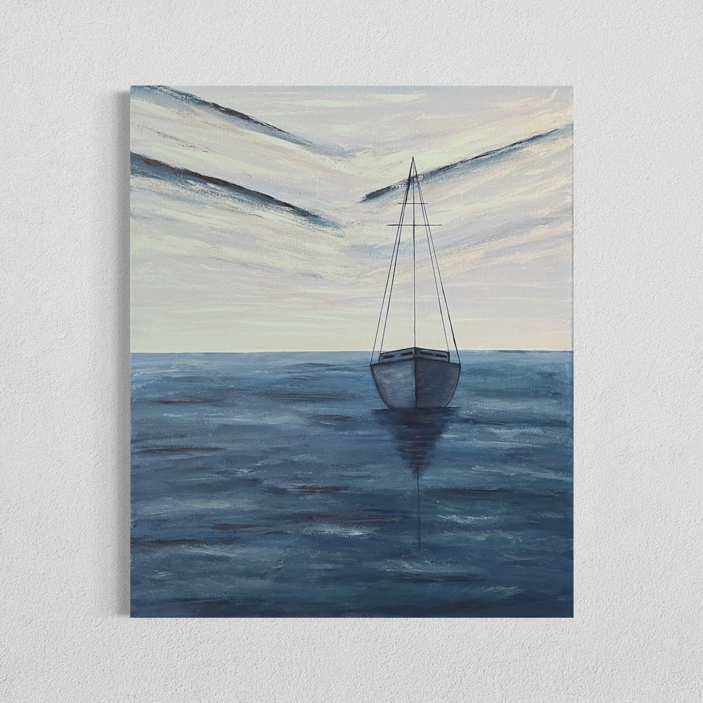 An affordable serene ocean painting of a solitary sailboat floating on calm, deep blue waters. The boat is slightly off center in the composition, with its reflection subtly visible on the water’s surface. The sky above is painted with soft, muted tones of pale blue, white and navy, with expressive brushstrokes forming abstract cloud patterns. The horizon line is faint, blending seamlessly with the sky and sea, creating a tranquil and minimalist atmosphere. The wall decor hangs on a white wall.
