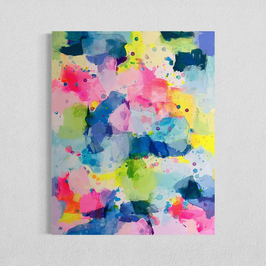 A happy, preppy affordable abstract painting featuring vibrant splashes of pink, blue, yellow, and green. The fluid brushstrokes and playful color combinations create a cheerful, energetic art composition with a watercolor-like effect. The layering of translucent hues and scattered paint splatters evoke a sense of lightness and spontaneity, embodying a bright and uplifting aesthetic for a dopamine boost. This preppy colorful maximalism wall decor hangs on a white wall.