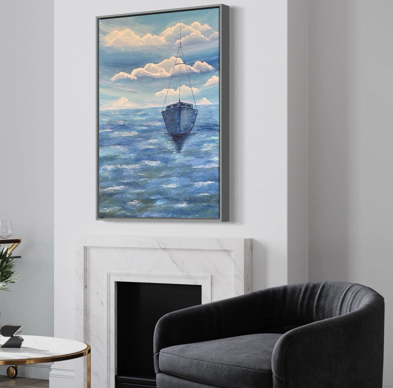 A serene ocean painting of a solitary sailboat floating on calm, deep blue waters. The boat is slightly off center in the composition, with its reflection subtly visible on the water’s surface. The sky above is painted with soft, muted tones of pale blue, white and navy, with expressive brushstrokes forming abstract cloud patterns. The horizon line is faint, blending seamlessly with the sky and sea, creating a tranquil and minimalist atmosphere. The art decor hangs on a white wall in a modern living room.