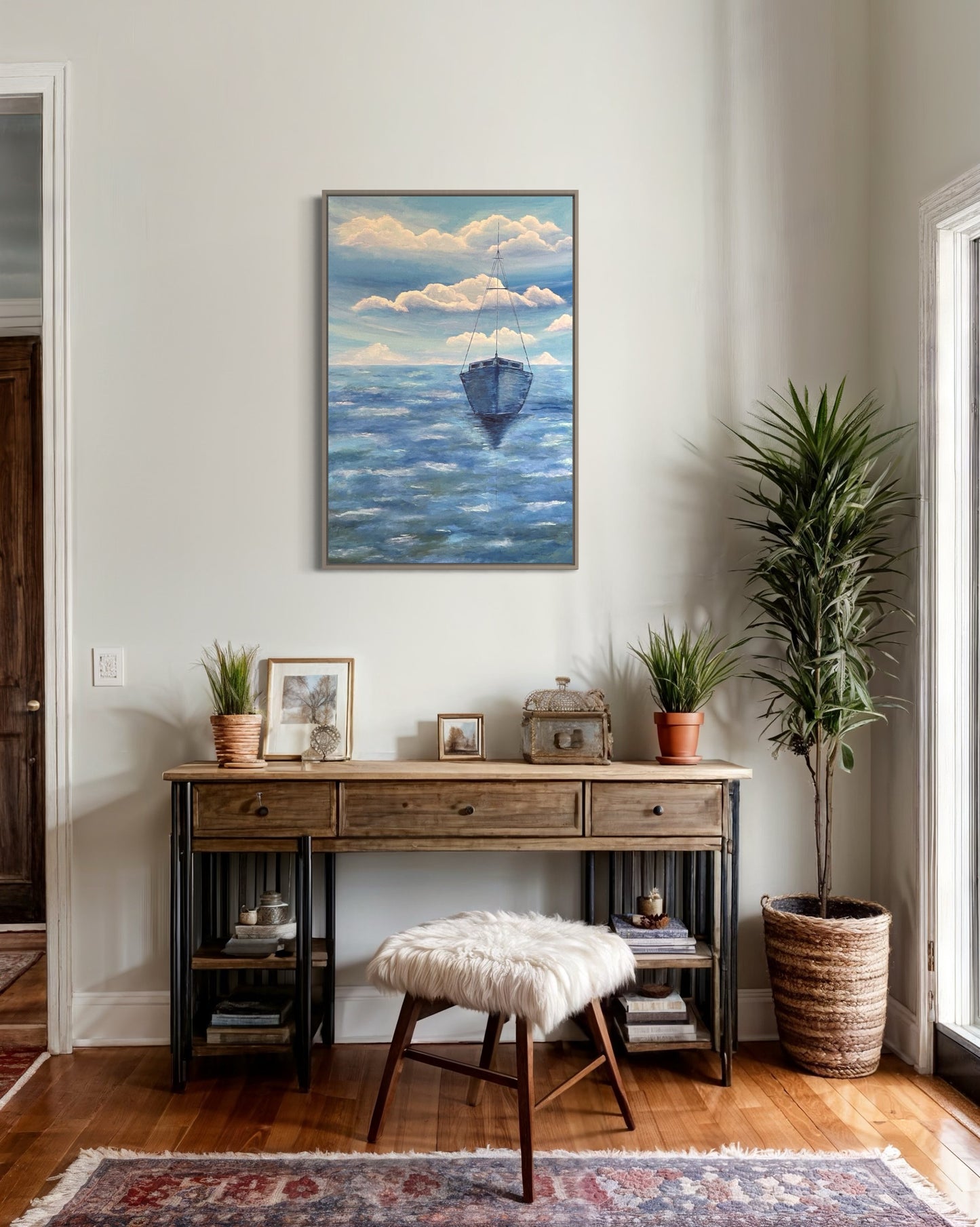A serene ocean painting of a solitary sailboat floating on calm, deep blue waters. The boat is slightly off center in the composition, with its reflection subtly visible on the water’s surface. The sky above is painted with soft, muted tones of pale blue, white and navy, with expressive brushstrokes forming abstract cloud patterns. The horizon line is faint, blending seamlessly with the sky and sea, creating a tranquil and minimalist atmosphere. The art decor hangs on a white wall in an entryway hallway.