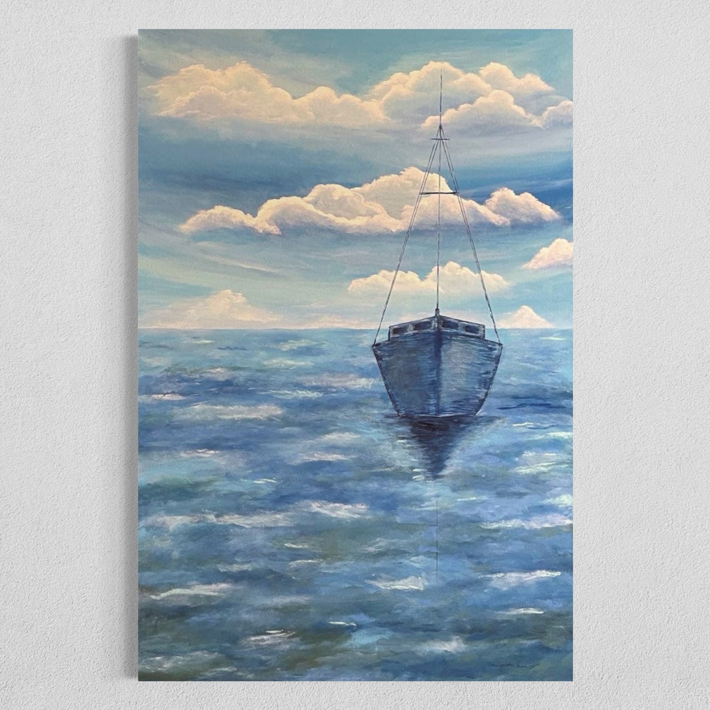 A serene ocean painting of a solitary sailboat floating on calm, deep blue waters. The boat is slightly off center in the composition, with its reflection subtly visible on the water’s surface. The sky above is painted with soft, muted tones of pale blue, white and navy, with expressive brushstrokes forming abstract cloud patterns. The horizon line is faint, blending seamlessly with the sky and sea, creating a tranquil and minimalist atmosphere. The art decor hangs on a white wall.