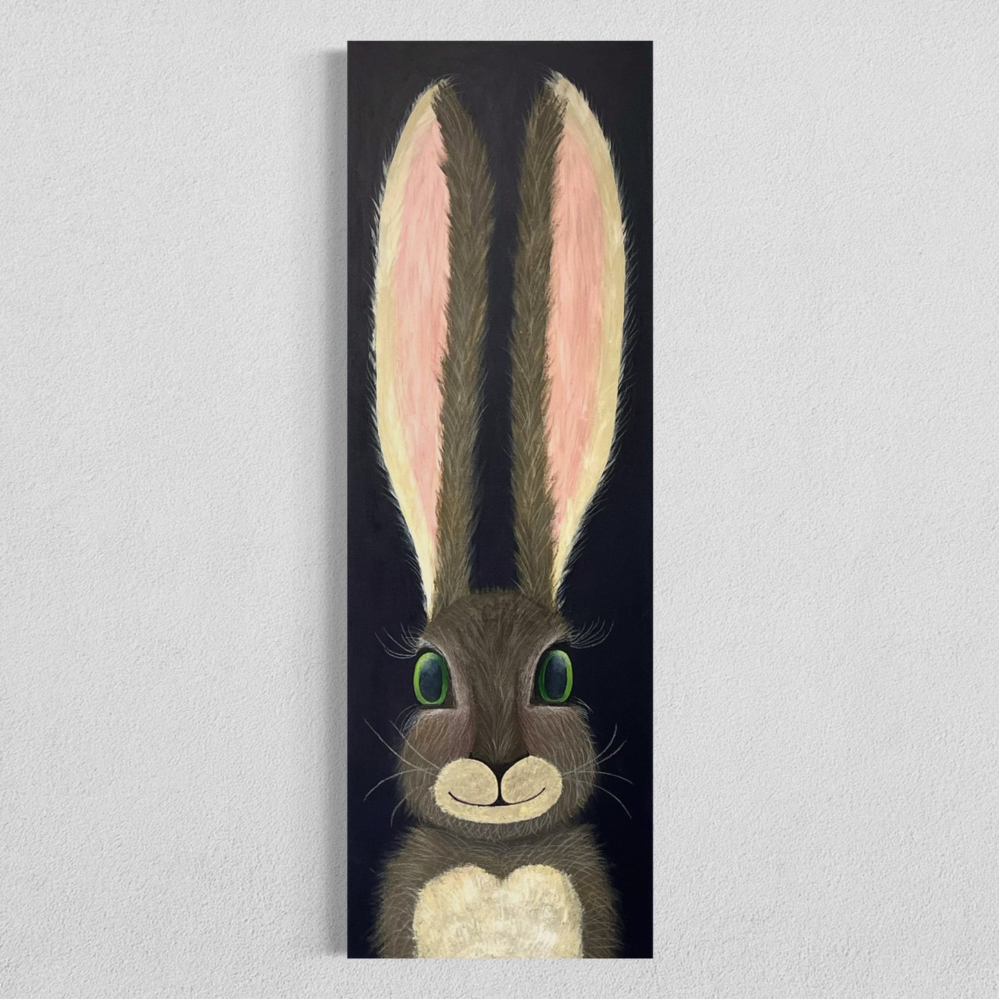 A 12"x36" oblong abstract acrylic painting with a cartoon style hare rabbit bunny with dazzling green eyes, gray and brown fur, pink ears, long eyelashes, on a navy blue background hangs on a white wall.