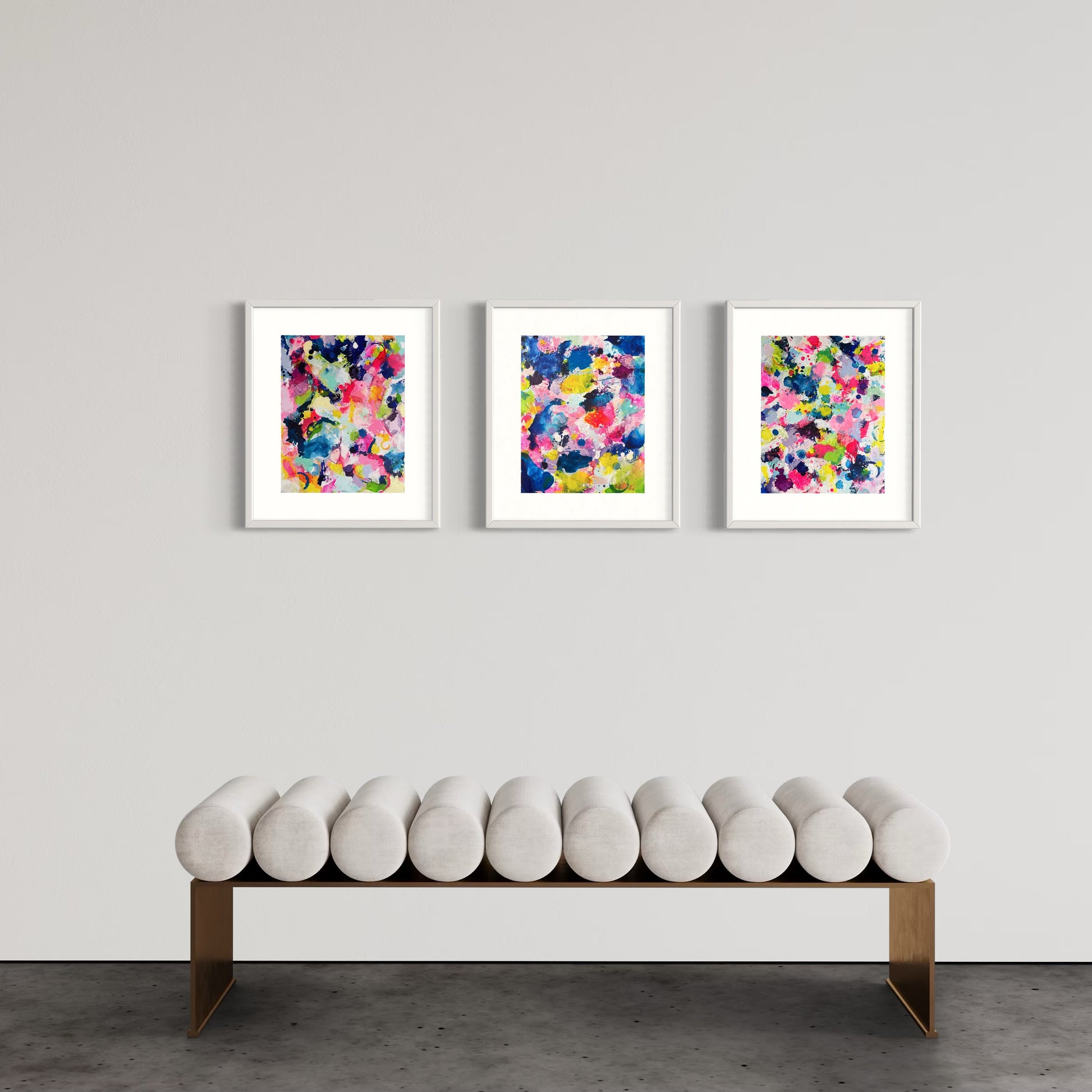 A modern gallery collection of abstract paintings featuring vibrant splashes of color, including pink, blue, yellow, green, purple and white. Each canvas is filled with expressive, energetic brushstrokes and layered paint splatters, creating a dynamic and contemporary composition. The affordable wall decor is arranged side by side on a white wall, forming a cohesive yet varied visual experience.