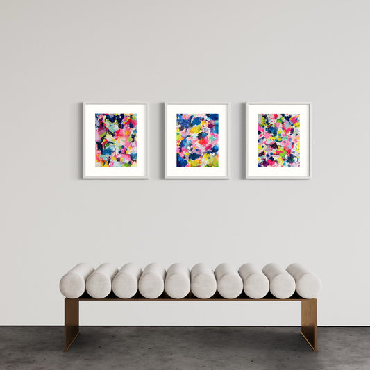 A modern gallery collection of abstract paintings featuring vibrant splashes of color, including pink, blue, yellow, green, purple and white. Each canvas is filled with expressive, energetic brushstrokes and layered paint splatters, creating a dynamic and contemporary composition. The affordable wall decor is arranged side by side on a white wall, forming a cohesive yet varied visual experience.