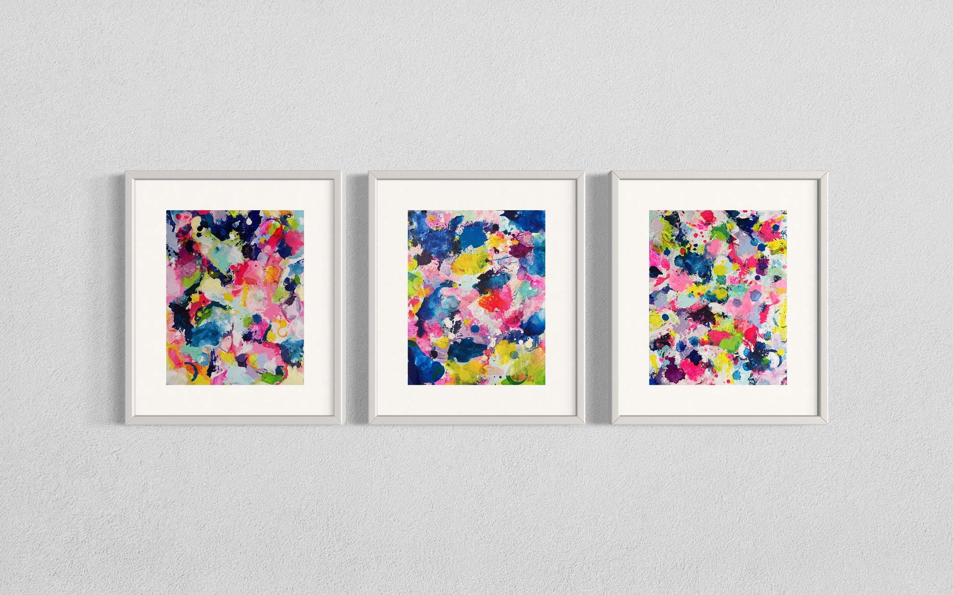 A modern gallery collection of abstract paintings featuring vibrant splashes of color, including pink, blue, yellow, green, purple and white. Each canvas is filled with expressive, energetic brushstrokes and layered paint splatters, creating a dynamic and contemporary composition. The affordable wall decor is arranged side by side on a white wall, forming a cohesive yet varied visual experience.