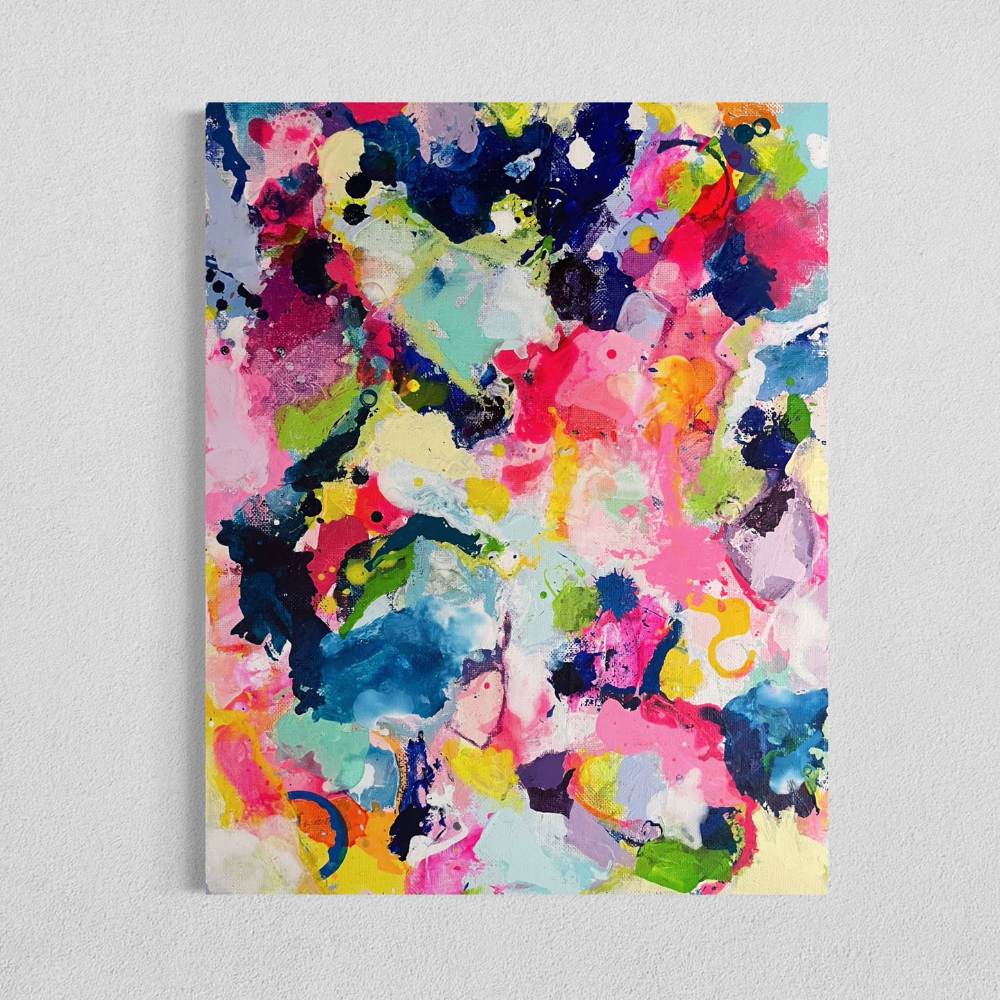 A modern gallery collection of abstract paintings featuring vibrant splashes of color, including pink, blue, yellow, green, purple and white. Each canvas is filled with expressive, energetic brushstrokes and layered paint splatters, creating a dynamic and contemporary composition. The affordable wall decor is arranged side by side on a white wall, forming a cohesive yet varied visual experience.