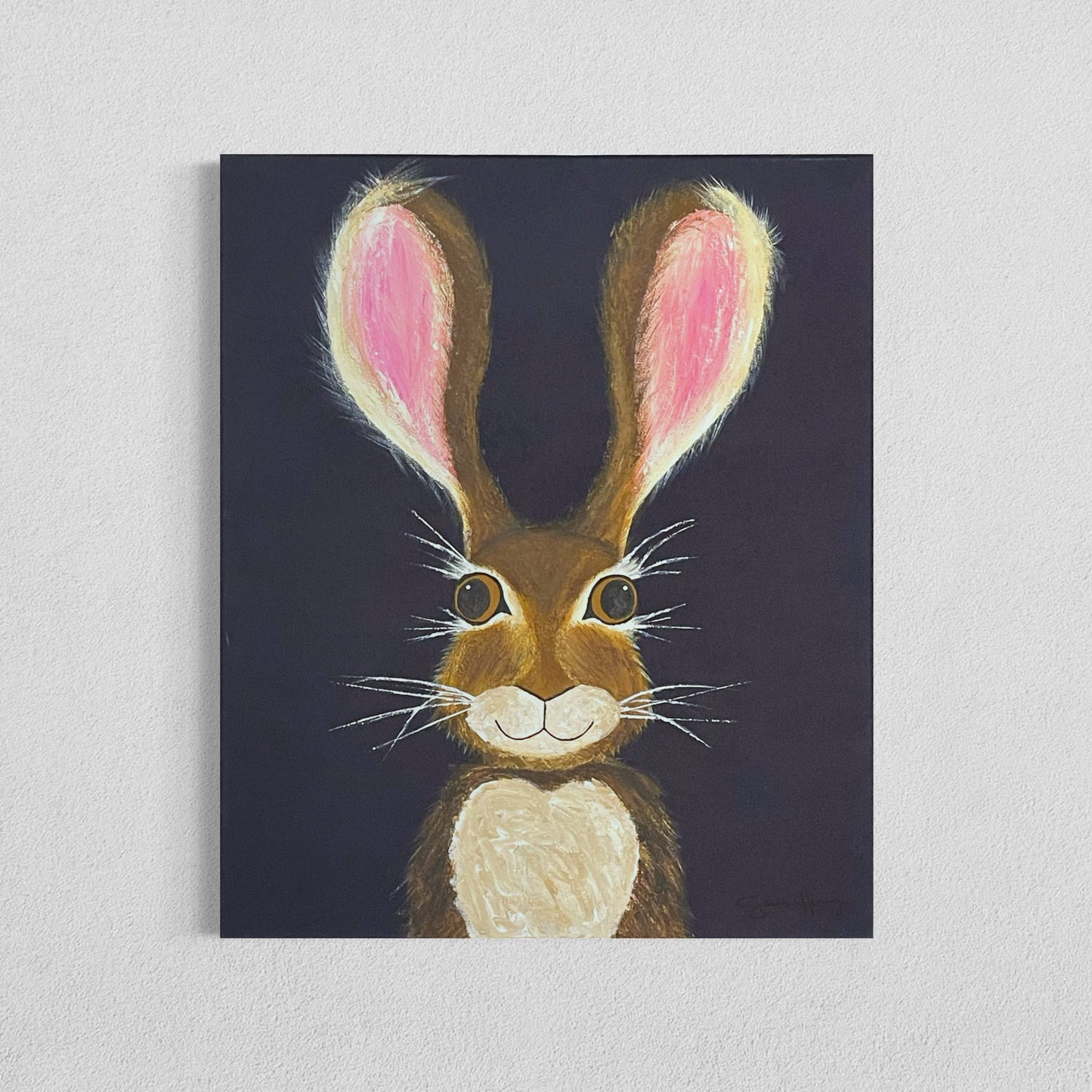 A 20"x24" affordable abstract acrylic painting with a cartoon style hare rabbit bunny with dazzling gold eyes, brown fur, pink ears, long eyelashes, on a navy blue background hangs on a white wall.