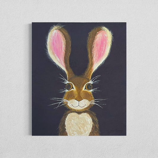 A 20"x24" affordable abstract acrylic painting with a cartoon style hare rabbit bunny with dazzling gold eyes, brown fur, pink ears, long eyelashes, on a navy blue background hangs on a white wall.