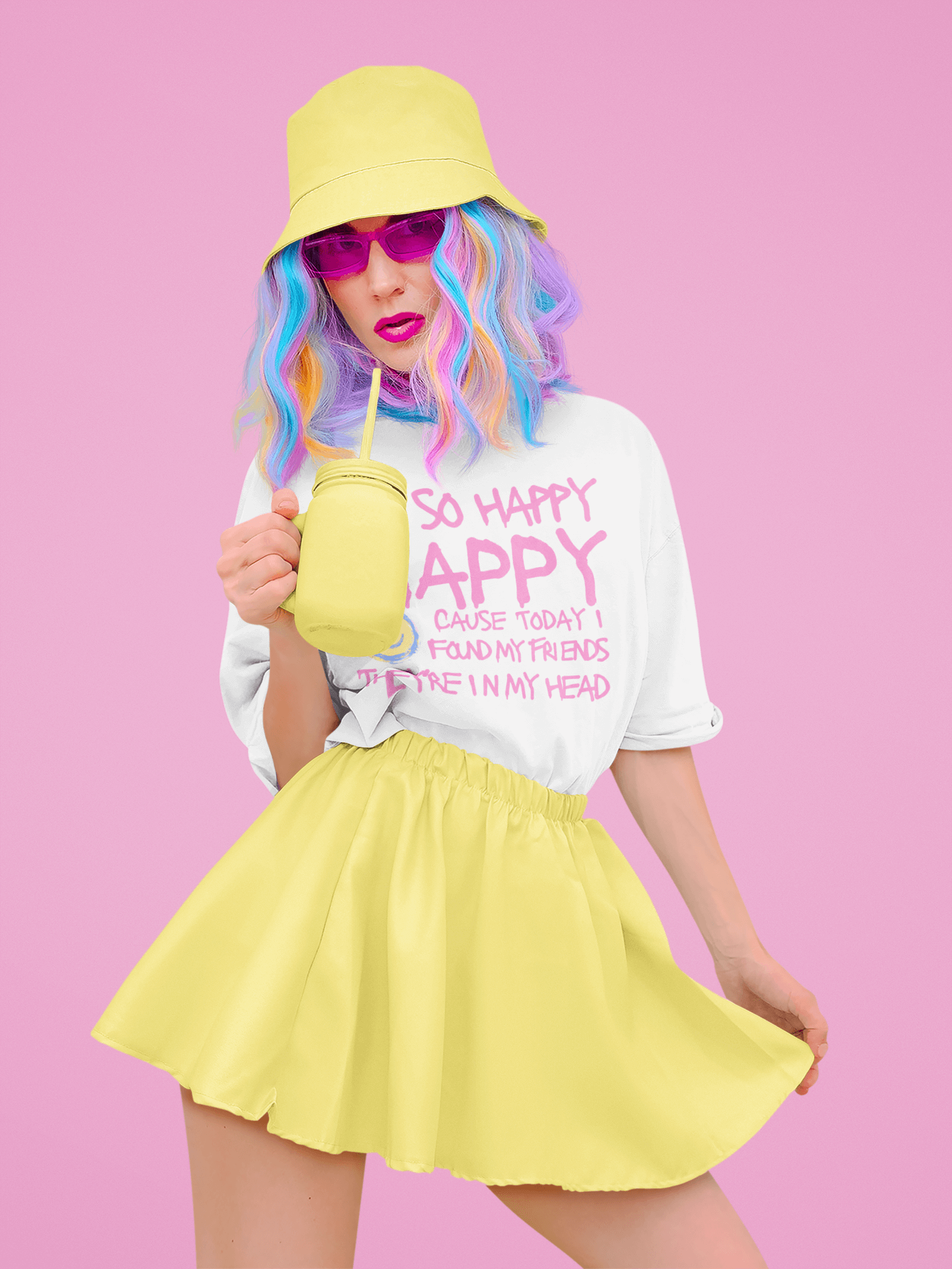 A stylish woman dressed in dopamine wearing an eclectic pastel yellow bucket hat and skirt, a white graphic T-shirt with Nirvana lyrics in pink text, and pink-tinted sunglasses. She has vibrant, multicolored hair and sips from a yellow mason jar cup against a pink background.