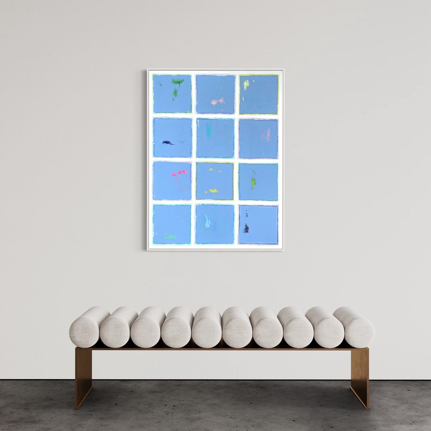 Modern abstract painting titled "Blue Cotton" featuring a grid of soft blue panels with colorful accents, bordered by white lines, hung above a minimalist bench on a neutral wall.