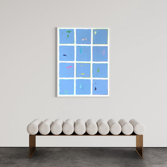 Modern abstract painting titled "Blue Cotton" featuring a grid of soft blue panels with colorful accents, bordered by white lines, hung above a minimalist bench on a neutral wall.