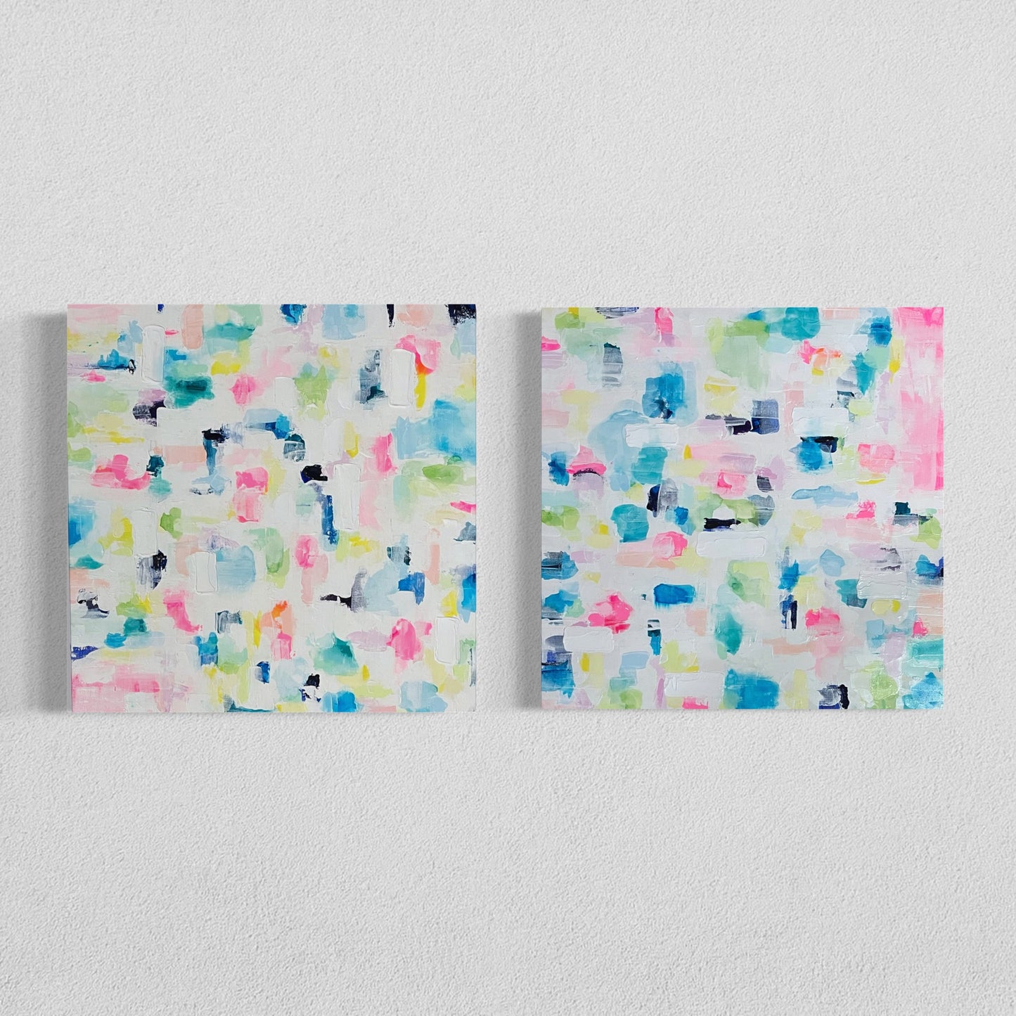 Two abstract pastel canvas paintings side by side on a white wall, featuring expressive brushstrokes in pink, blue, yellow, and green tones for modern home décor.